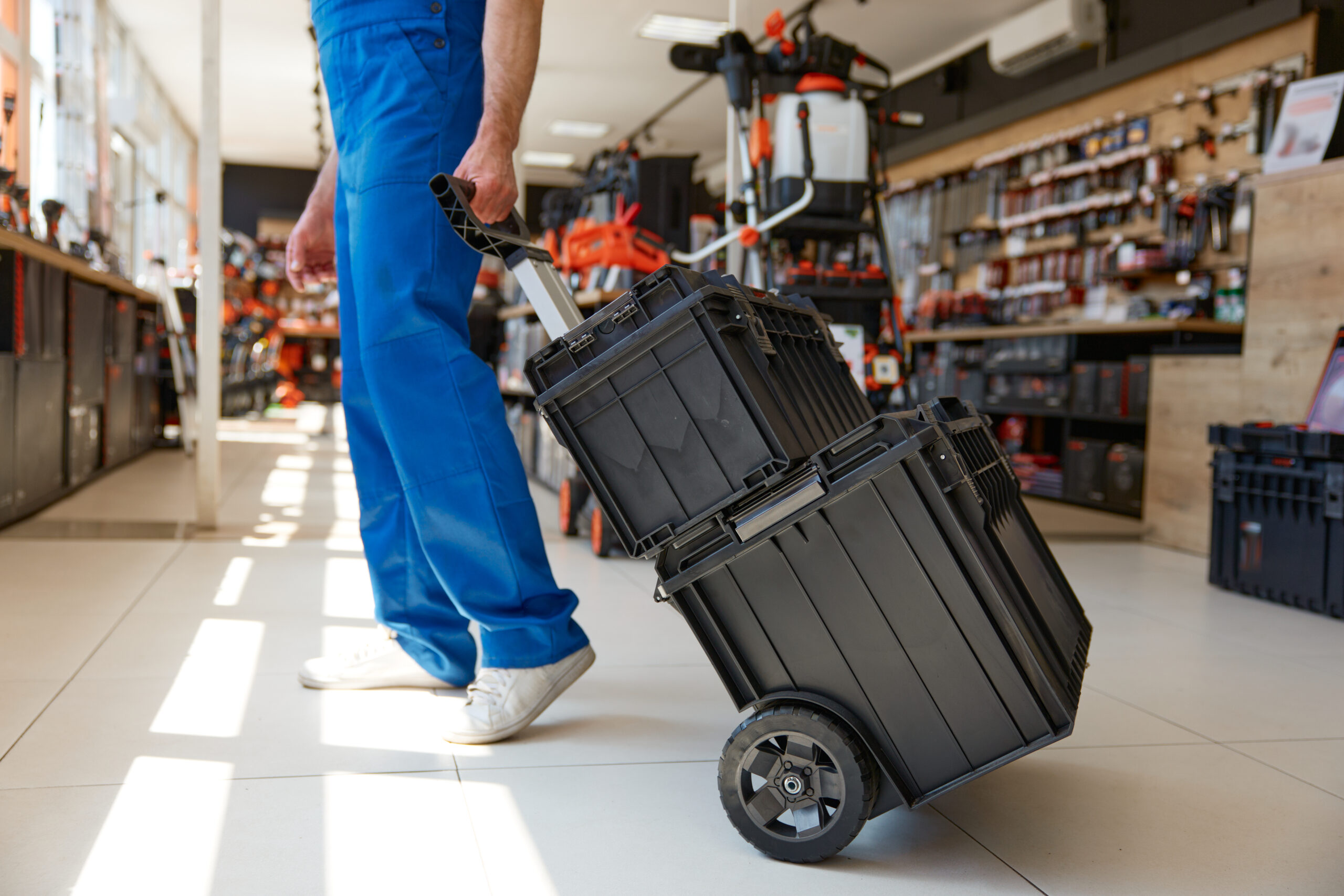 Handyman worker purchasing industrial tools kit at hardware store department. Satisfied repairman pushing trolley cart with new instruments in storage boxes